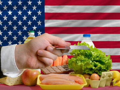 Man stretching out credit card to buy food in front of complete wavy national flag of usa
