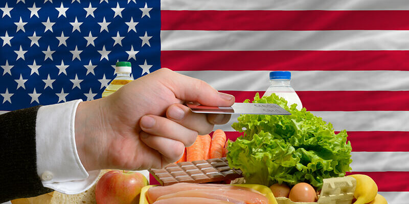 Man stretching out credit card to buy food in front of complete wavy national flag of usa