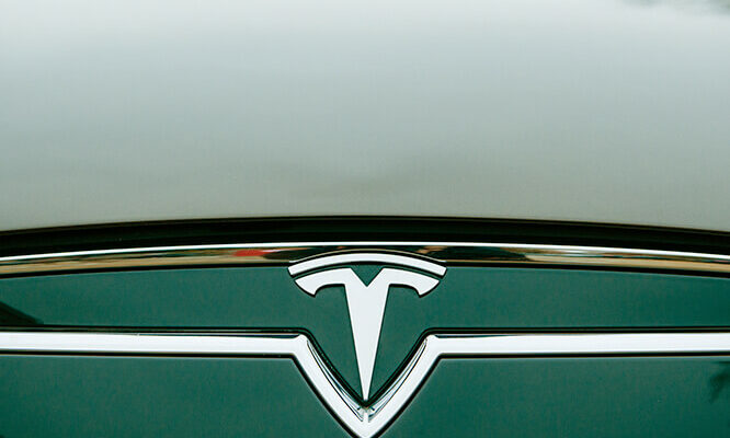 The Tesla Motors Inc. badge and logo are seen below the hood of the Model S electric vehicle