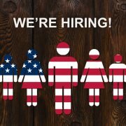 Paper men colorized into the color of the usa flag on wooden background with text WE'RE HIRING. Business concept.