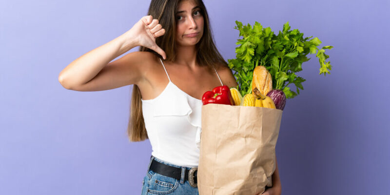 Young woman holding a grocery shopping bag showing thumb down with negative expression