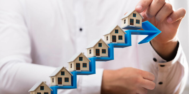 Close-up of a businessman's hand placing house models on increasing blue arrow staircase