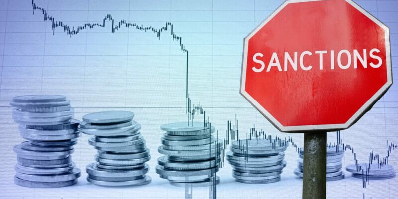 Sanctions sign against economy background with graph and coins.