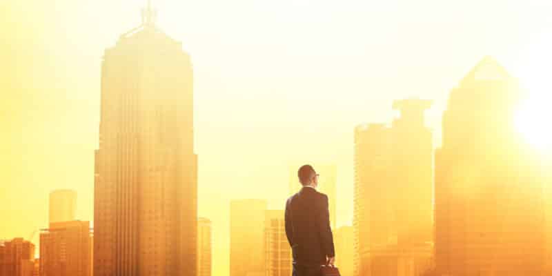 Young smart businessman looking at large city center. Concept of success and appreciation. Standing in front of the spectacular skyline with crowded corporate skyscrapers.