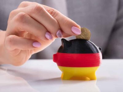 Woman's Hand Inserting Coin In Piggybank Painted With German Flag