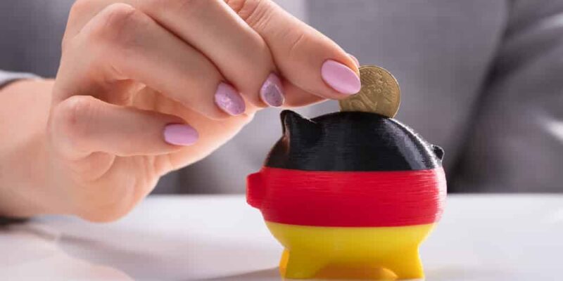 Woman's Hand Inserting Coin In Piggybank Painted With German Flag