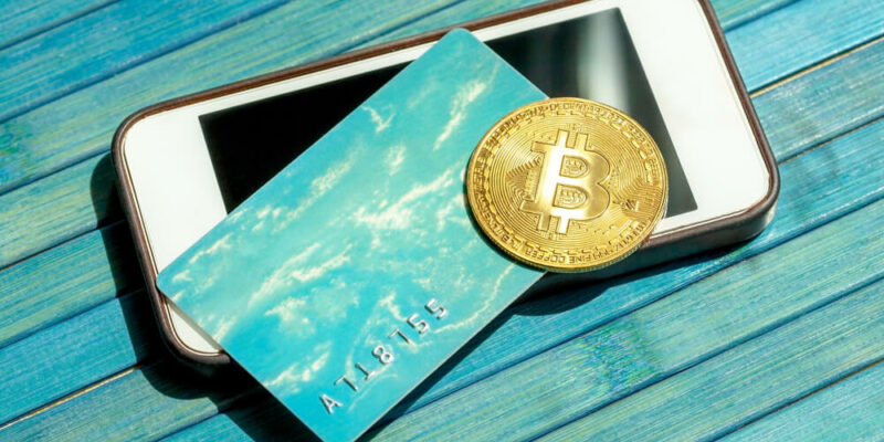 Bitcoin gold coin and a gift card, credit card laying on top of a modern smartphone screen. BTC blockchain payments, mobile portable storing and payment, paying with crypto currency abstract concept