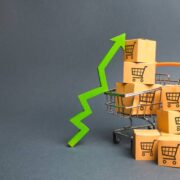 Shopping cart with cardboard boxes with a pattern of trading carts and a green up arrow. Increase the pace of sales, production of goods. Improving consumer sentiment. Strategy for increasing revenue