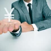 a businessman sitting in a desk showing a chinese yuan or japanese yen sign in his hand