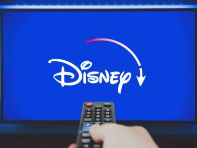 Man holds a remote control. Disney+ logo on TV screen in background.