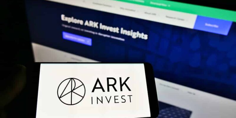 Person holding smartphone with logo of US asset manager ARK Investment Management LLC on screen in front of website. Focus on phone display.