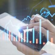 Close up of businessman hand pointing at pad on desktop with creative glowing forex chart on blurry outdoor background.